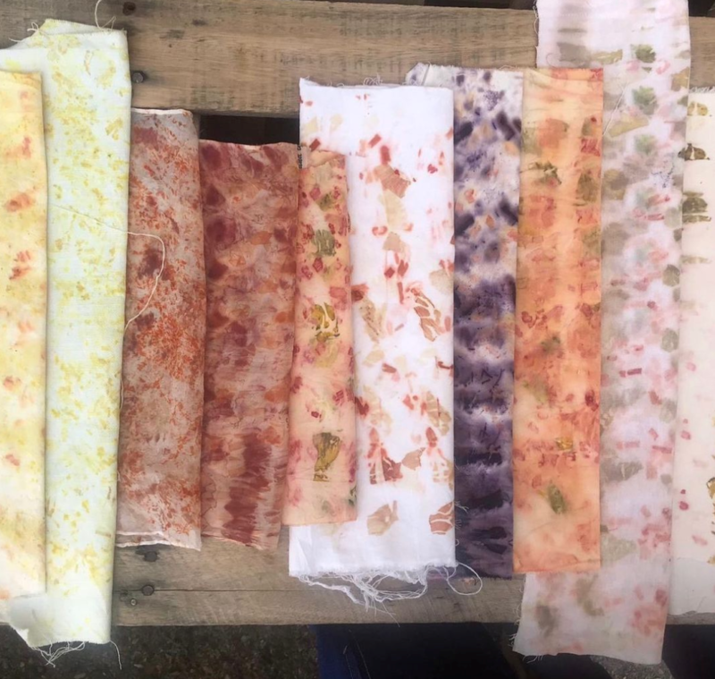 Rolls of fabric, dyed with natural colourings and decorated with flowery patterns. The textiles are laid flat on a wooden table. 